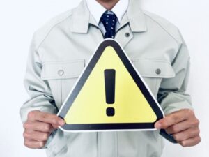 作業服の職人が警告サインを持つ注意喚起イメージ