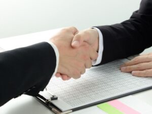 契約書の上で握手・業者との契約締結イメージ